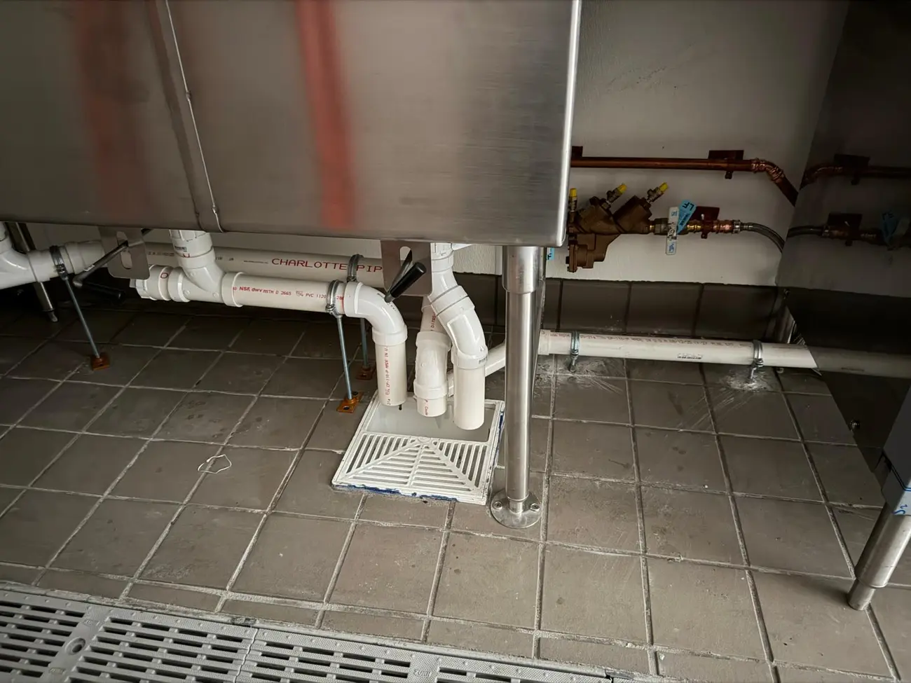 Commercial kitchen plumbing with stainless equipment and floor drains