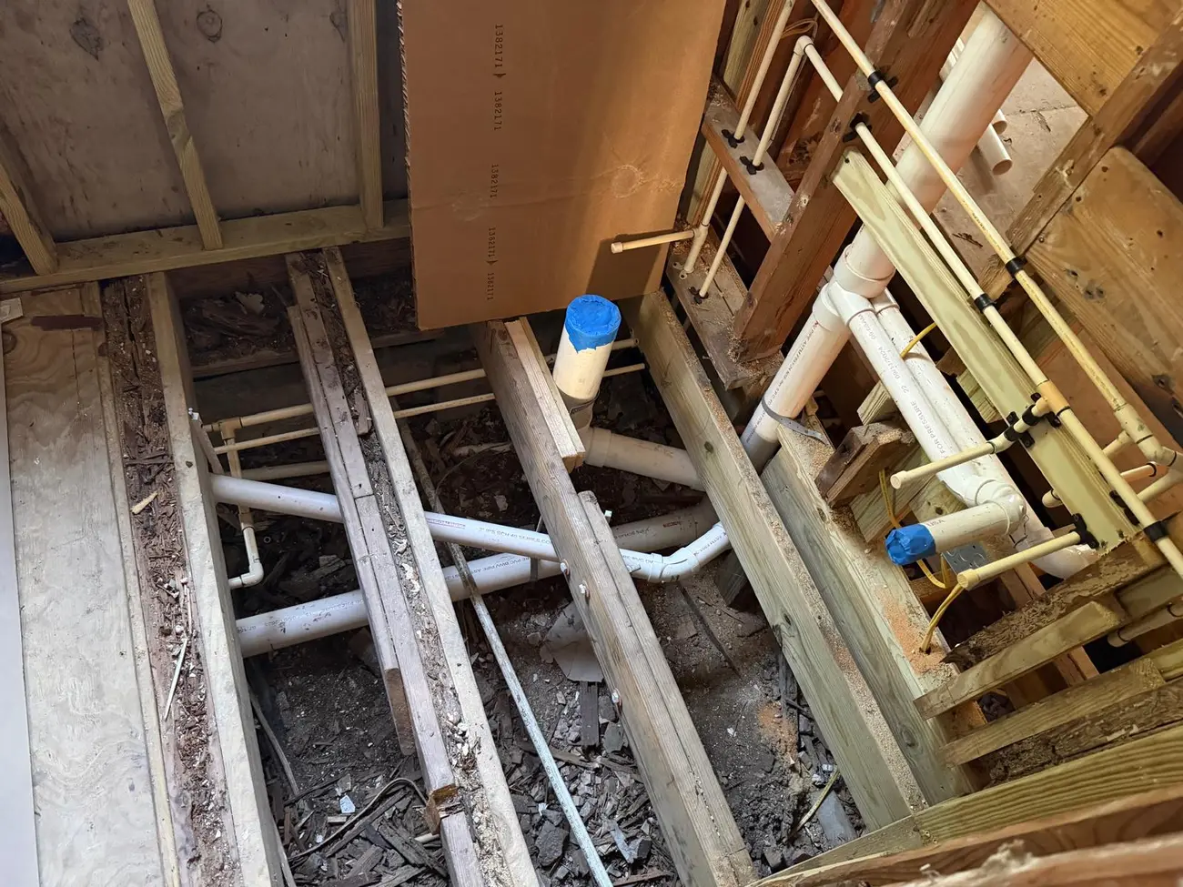 Bathroom floor rough-in with drain and supply lines between joists