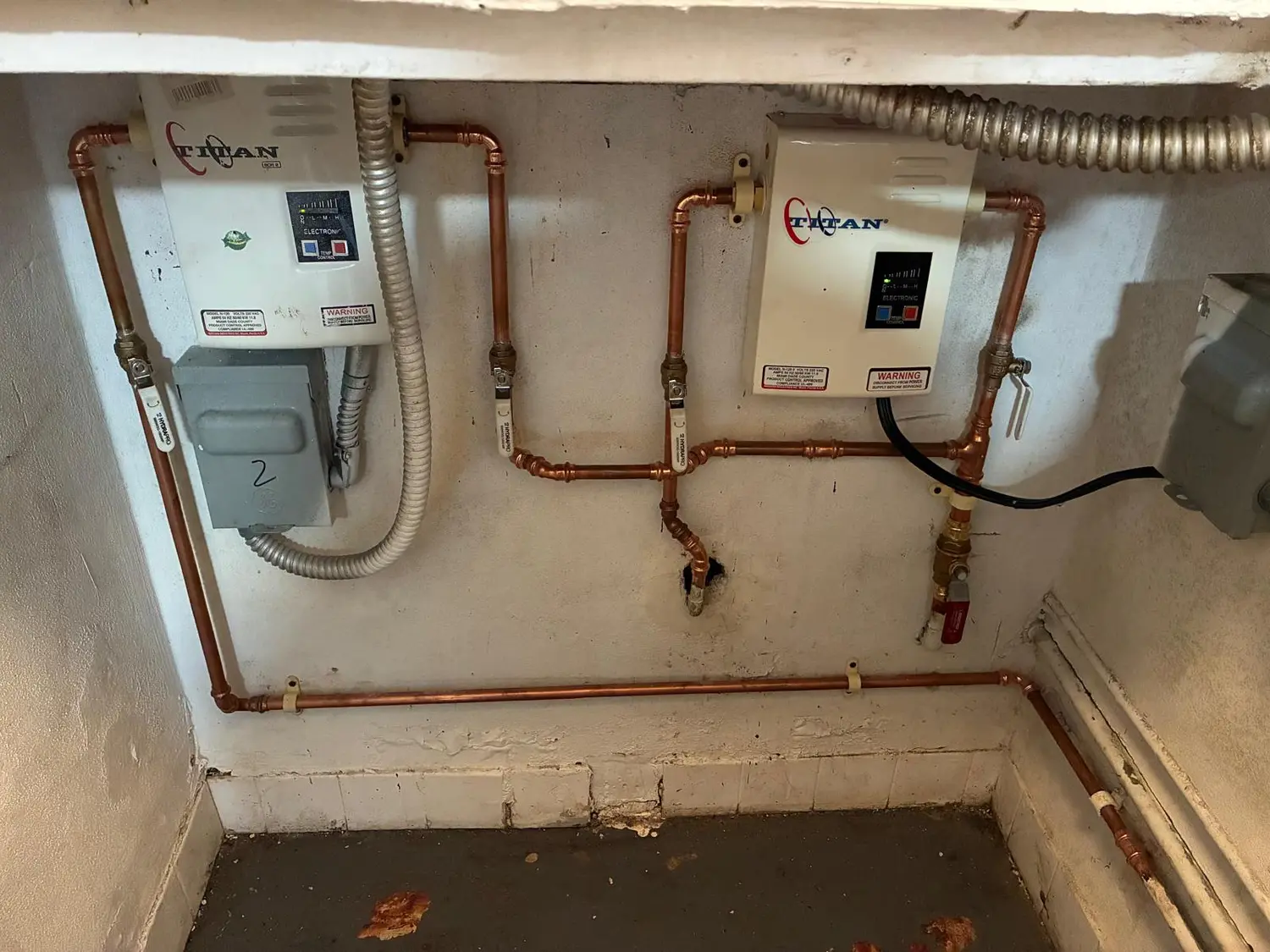 Two tankless water heaters with copper and gas piping on a commercial wall